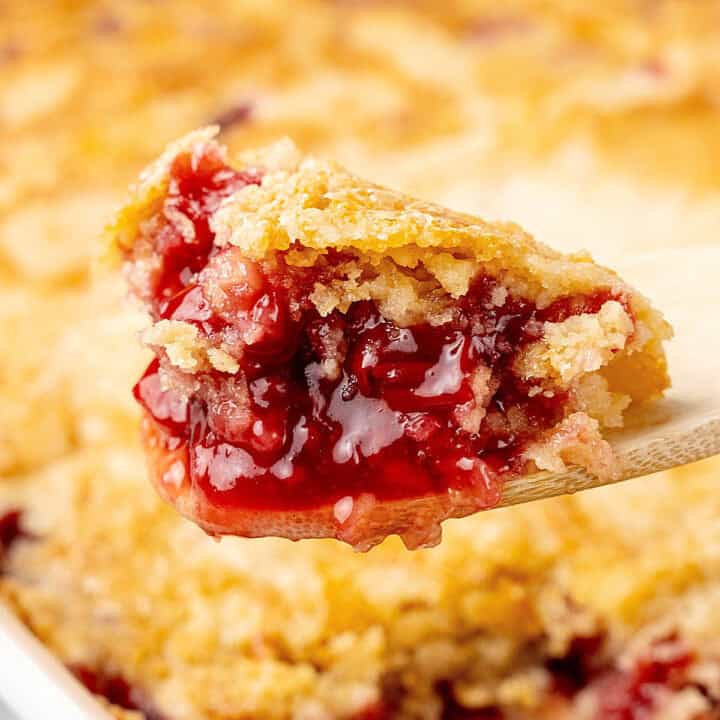 Close up of scooped portion of cherry dump cake on a wooden spoon.