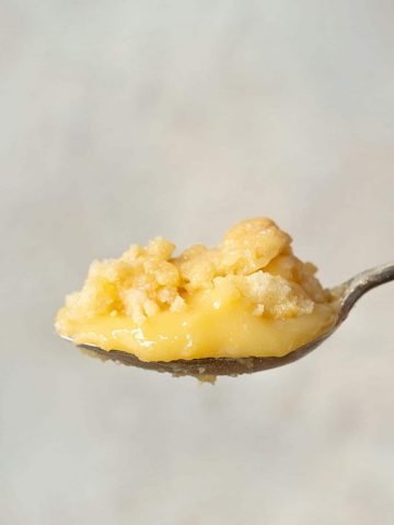 Spoon with serving of lemon dump cake against a grey background.