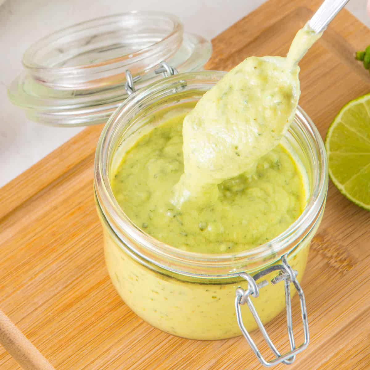 Spooning avocado lime dressing from a mason jar on a wooden board. 