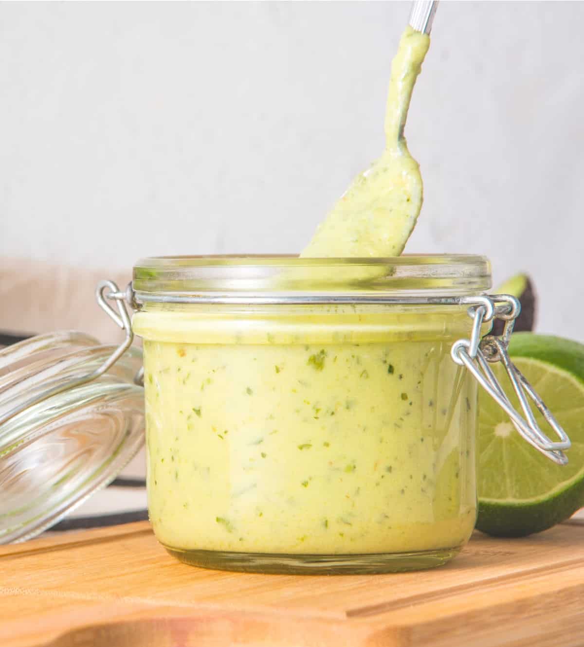 Lifting a spoon from a mason jar with avocado ranch dressing on a wooden board. 