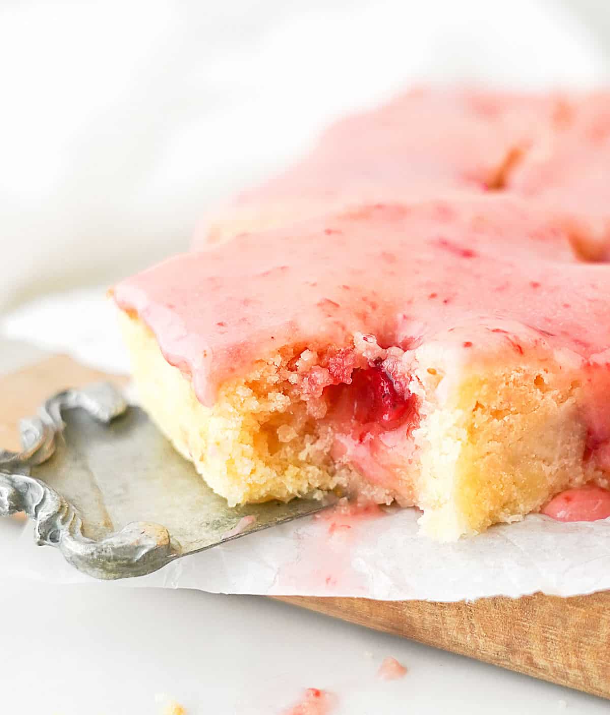 Bitten glazed lemon strawberry blondie being lifted on a vintage cake server from parchment paper. White background.