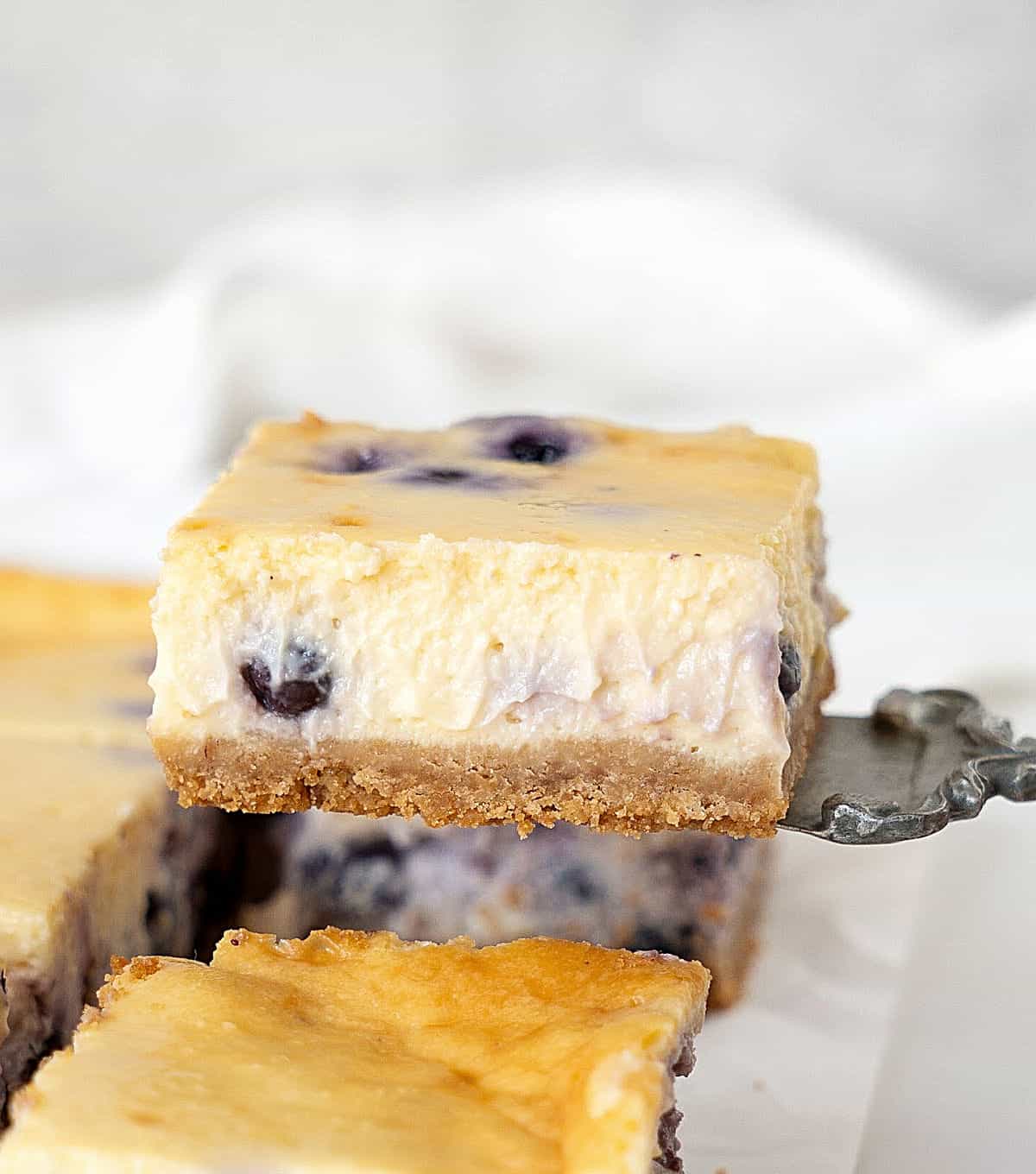 Lifting a square of blueberry cheesecake bars with a vintage server. White and light grey background.
