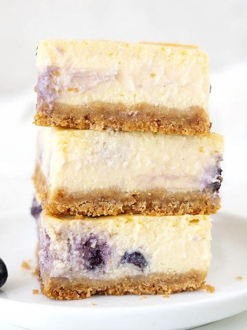 White plate with stack of three blueberry cheesecake squares. White grey background.