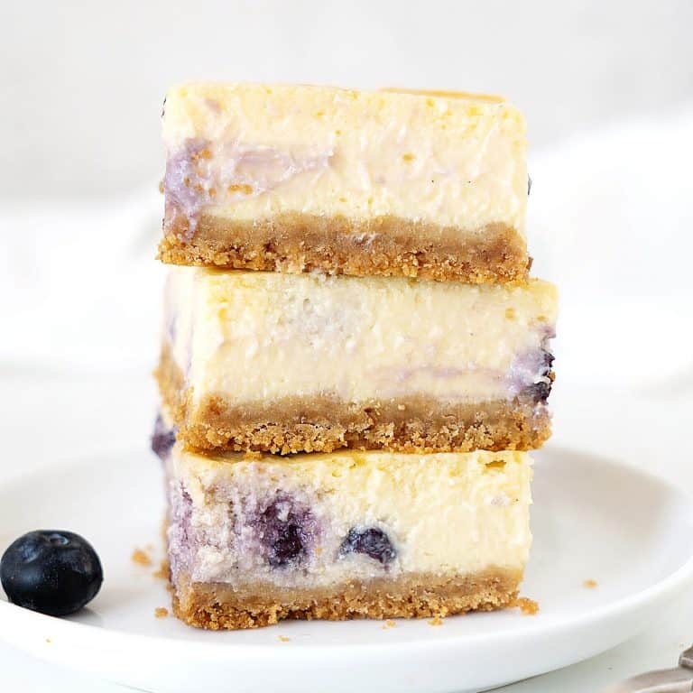 White plate with stack of three blueberry cheesecake squares. White grey background.