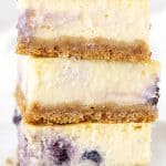Close up of stack of three blueberry cheesecake bars with white background. Purple text overlay.
