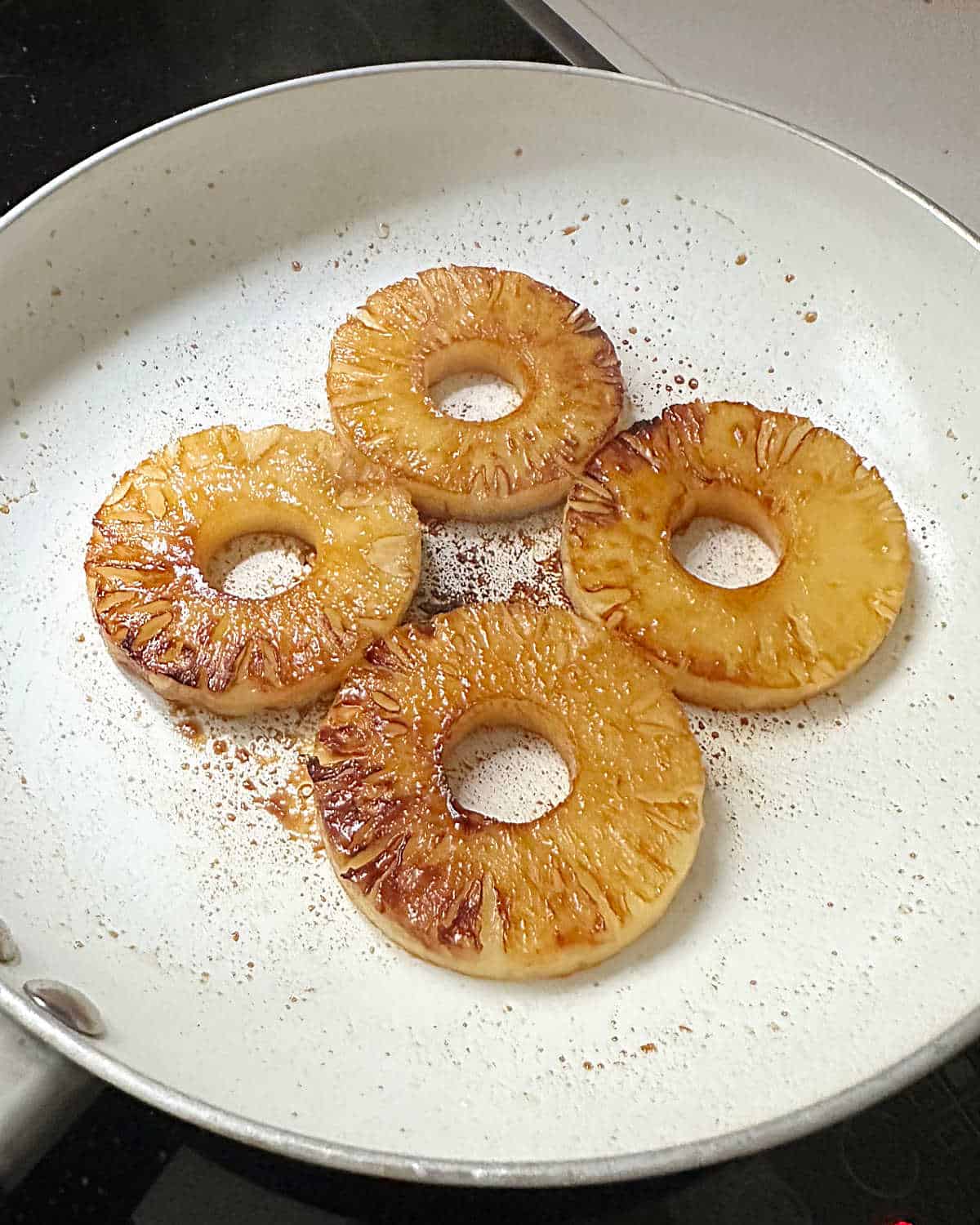 White skillet with caramelized pineapple rounds.