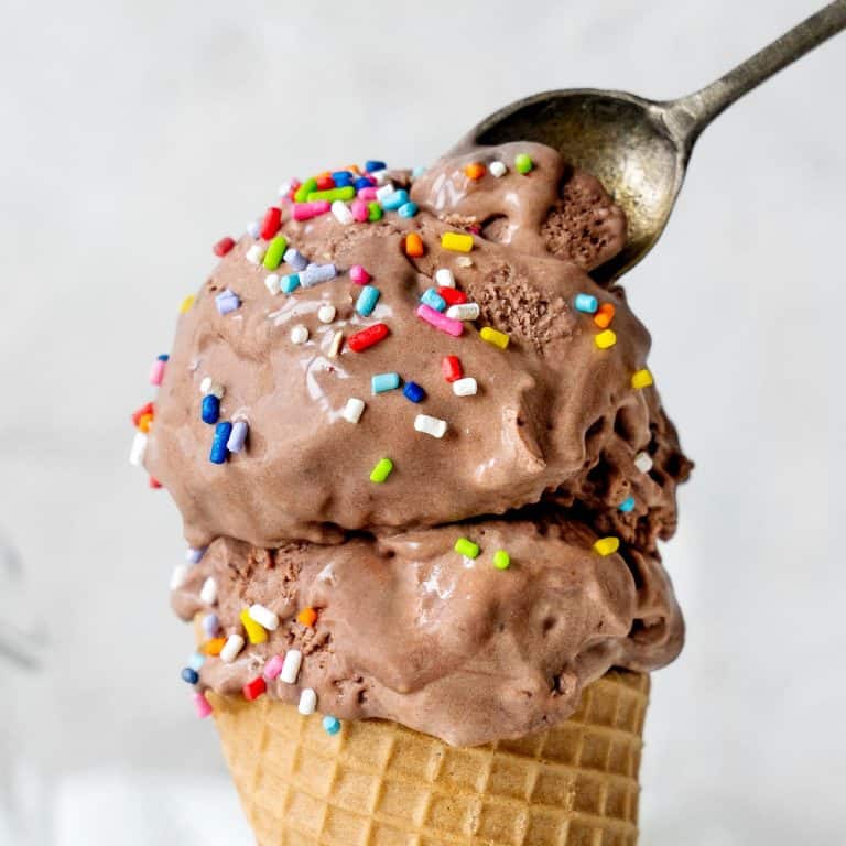A waffle cone with scoops of chocolate ice cream with sprinkles. Grey background, vintage spoon.