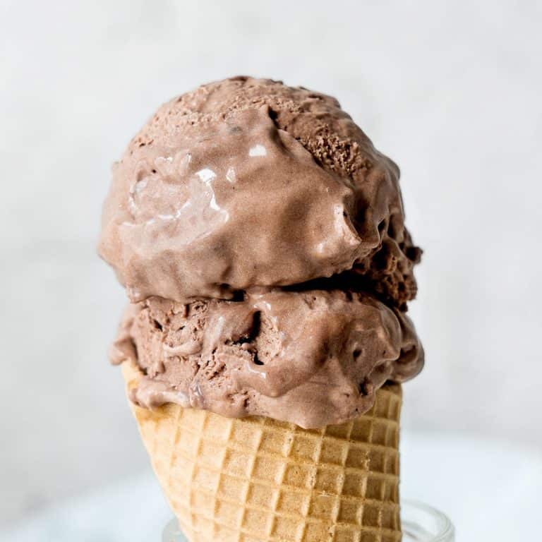 Two scoops of chocolate ice cream on a waffle cone with a light grey background.