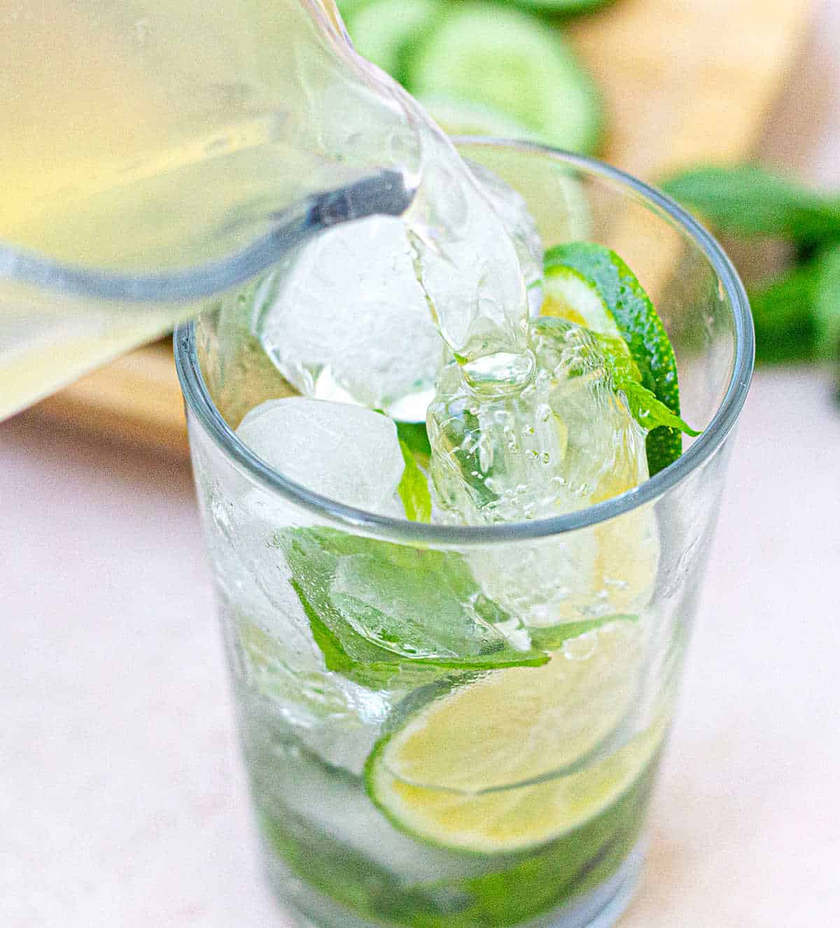 Pouring cucumber lime water into glass with ice, lime and cucumber slices.