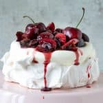 Cherry cream pavlova on a pink cake stand with grey background.