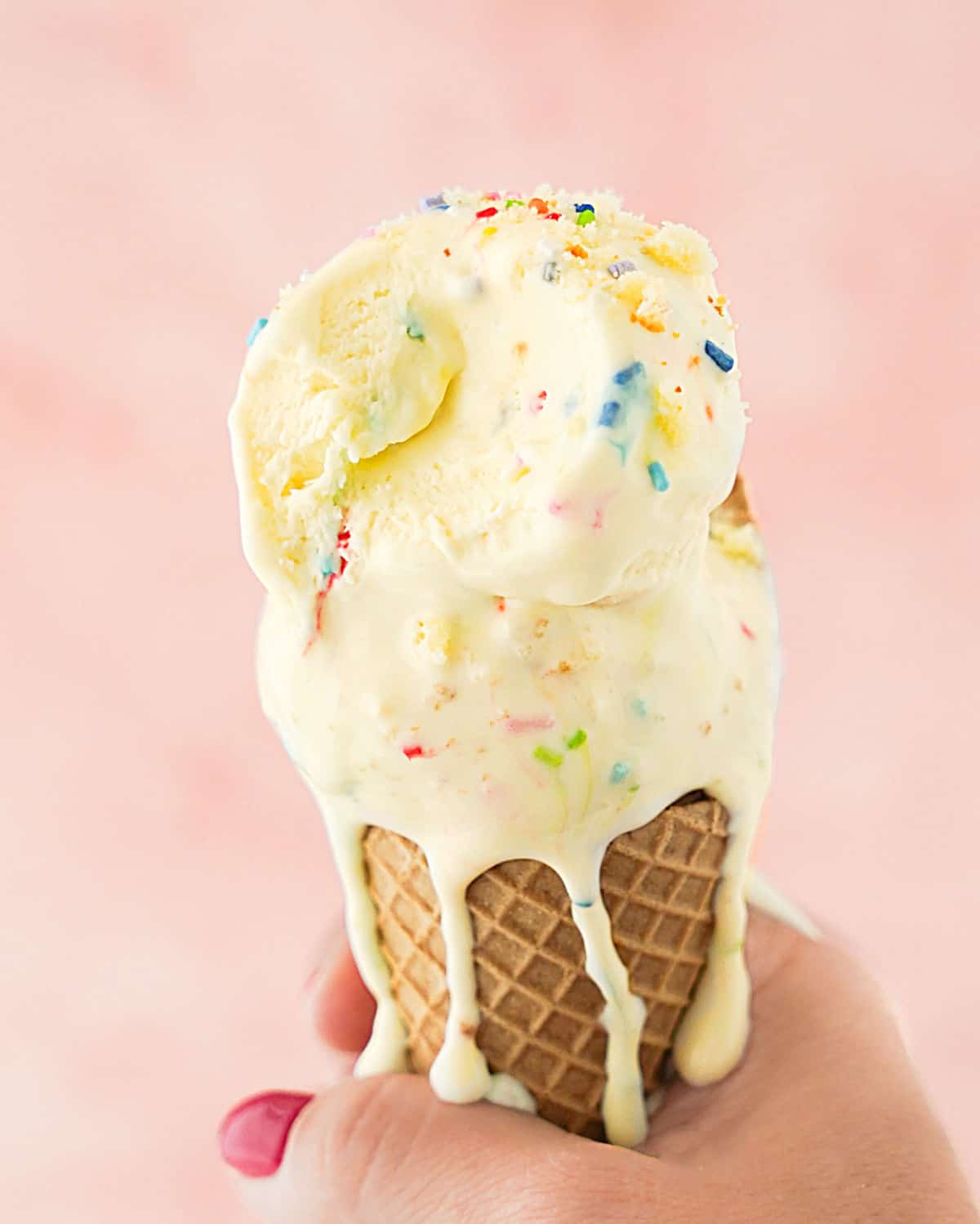 Pink background with hand holding funfetti ice cream waffle cone. 