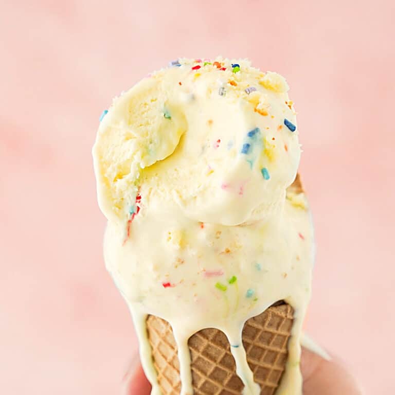 Close up of funfetti ice cream in a waffle cone. Pink background.