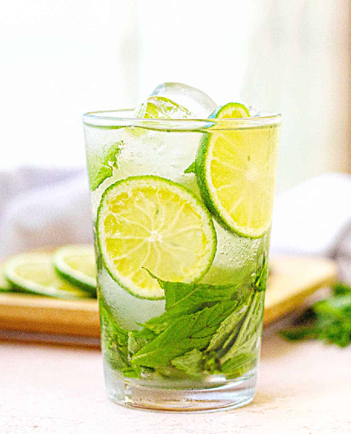 Singles glass with cucumber lime water and mint leaves. Light colored background.
