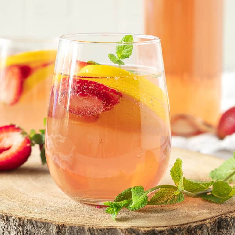 Glasses of rosé wine sangria with strawberries and orange slices on a wood board. Mint leaves.