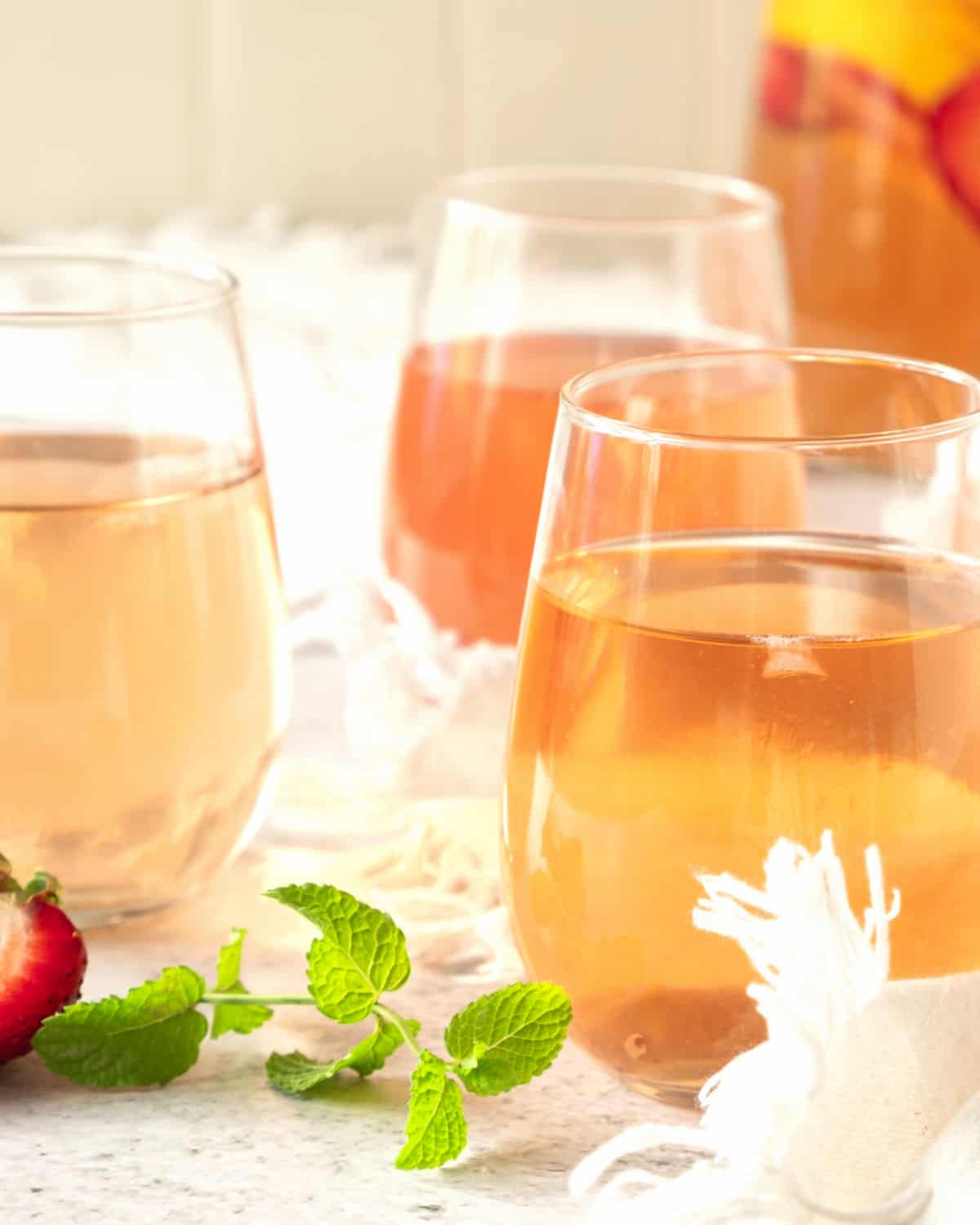 Three glasses with rose sangria, no fruit. White beige background with pitcher. Mint leaves.