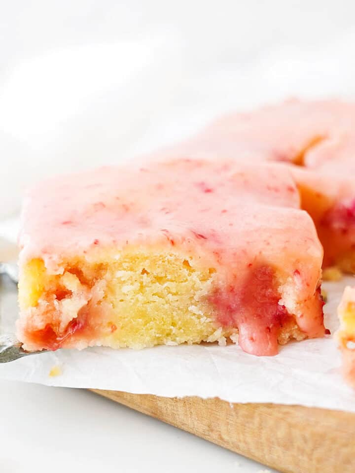 Glazed strawberry lemon blondie on parchment paper and wooden board. White background.