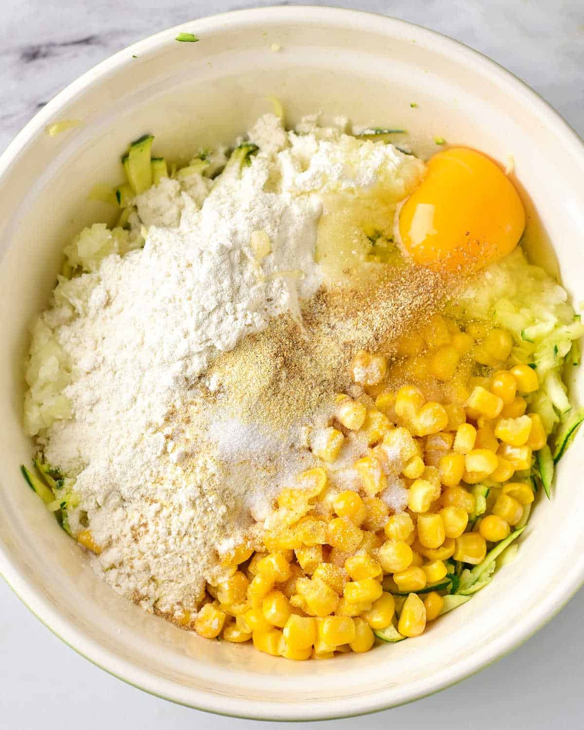 Close up of zucchini corn fritter ingredients in a cream-colored bowl.