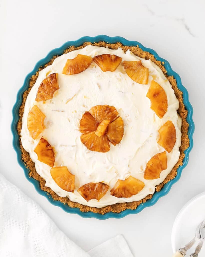 Whole pineapple cream cheese pie in a teal dish. Top view on a white surface.