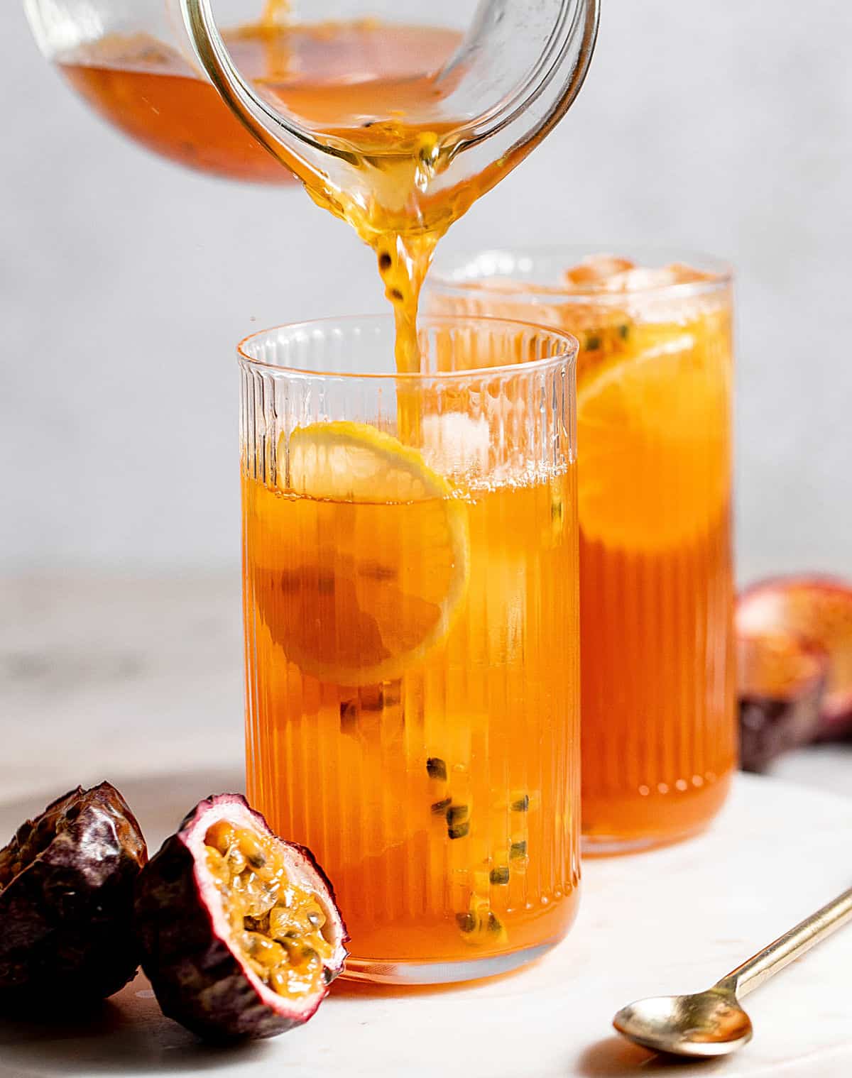 Serving passionfruit tea in tall glasses on a marble surface. Grey background, fresh passionfruit halves.