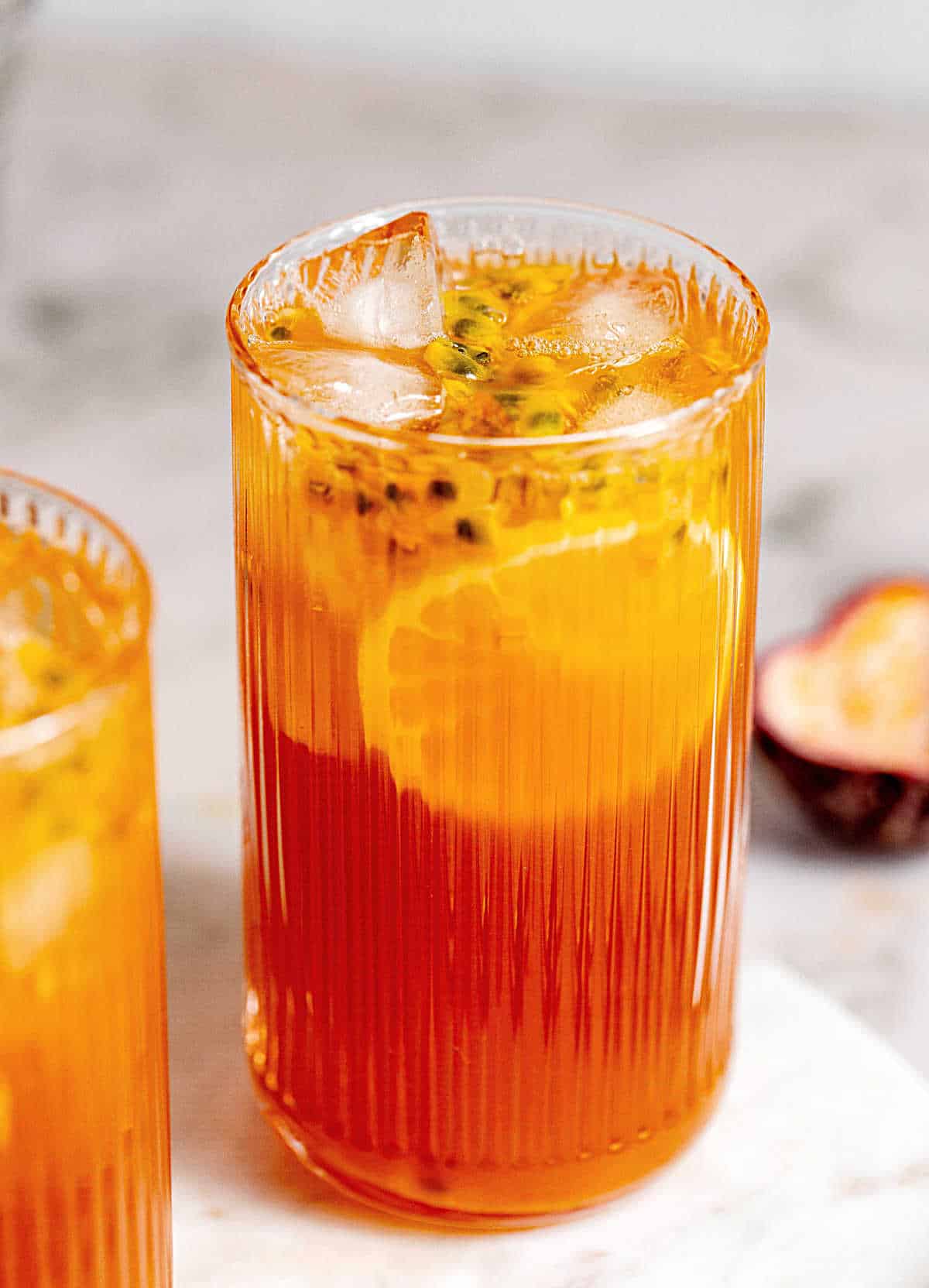 Tall glass of passionfruit tea on a marble board with grey background.
