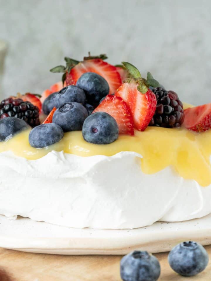 Lemon and berries pavlova on a wooden surface with grey background.