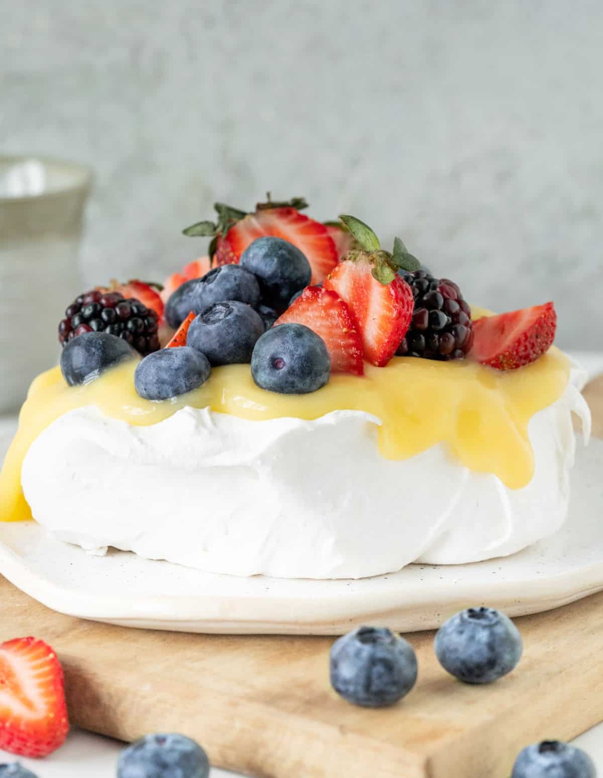 Pavlova with lemon curd and fresh berries on wooden board with grey background. 