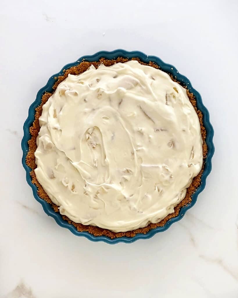 Filled crumb crust with pineapple cream cheese mixture. White marbled surface.