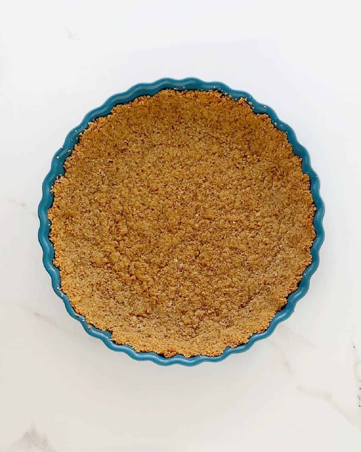 Graham cracker crust on a teal round pie dish. White marbled surface.