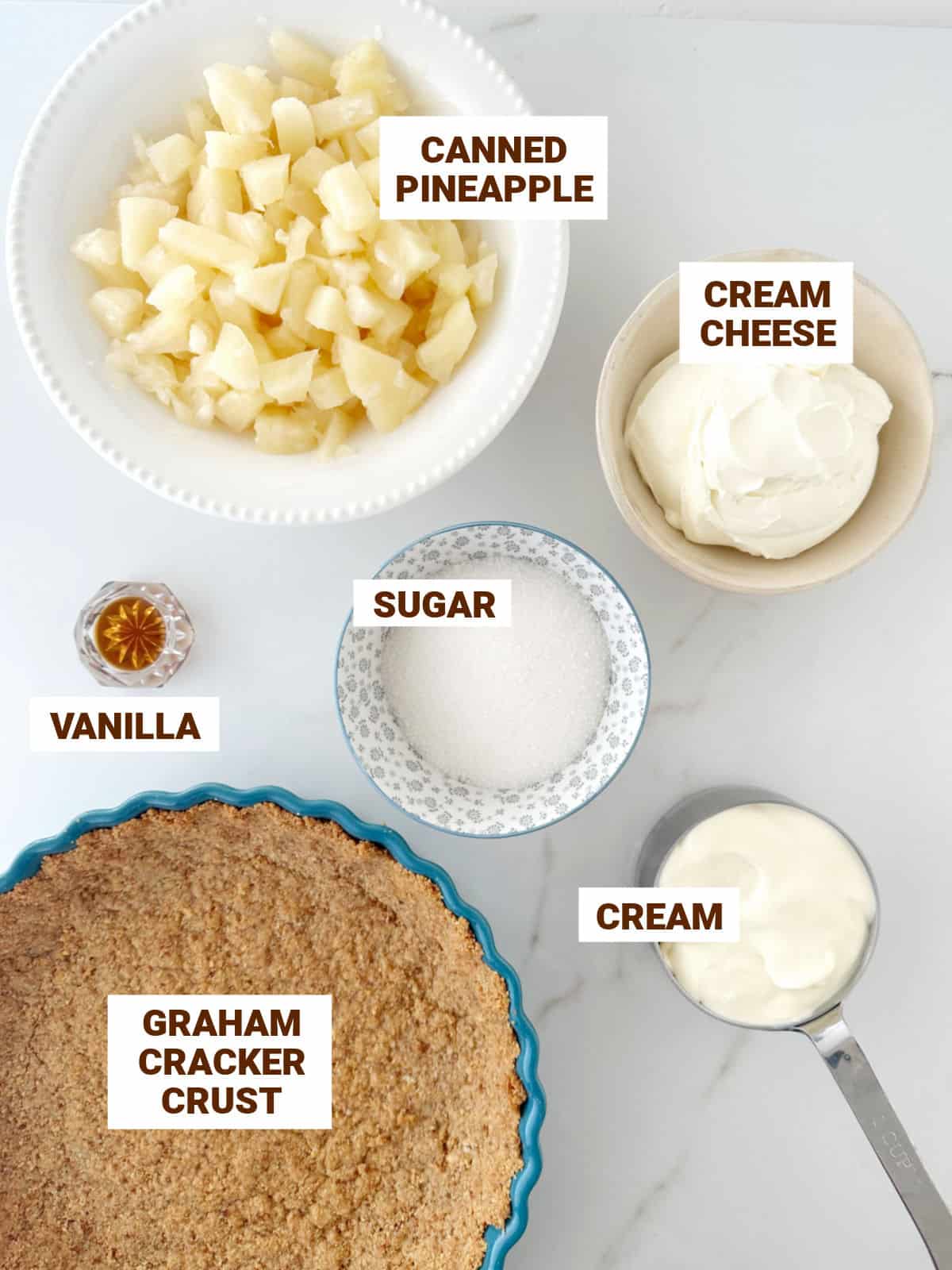 Pineapple cream cheese pie ingredients on a white surface including graham crust, sugar, vanilla, cream.