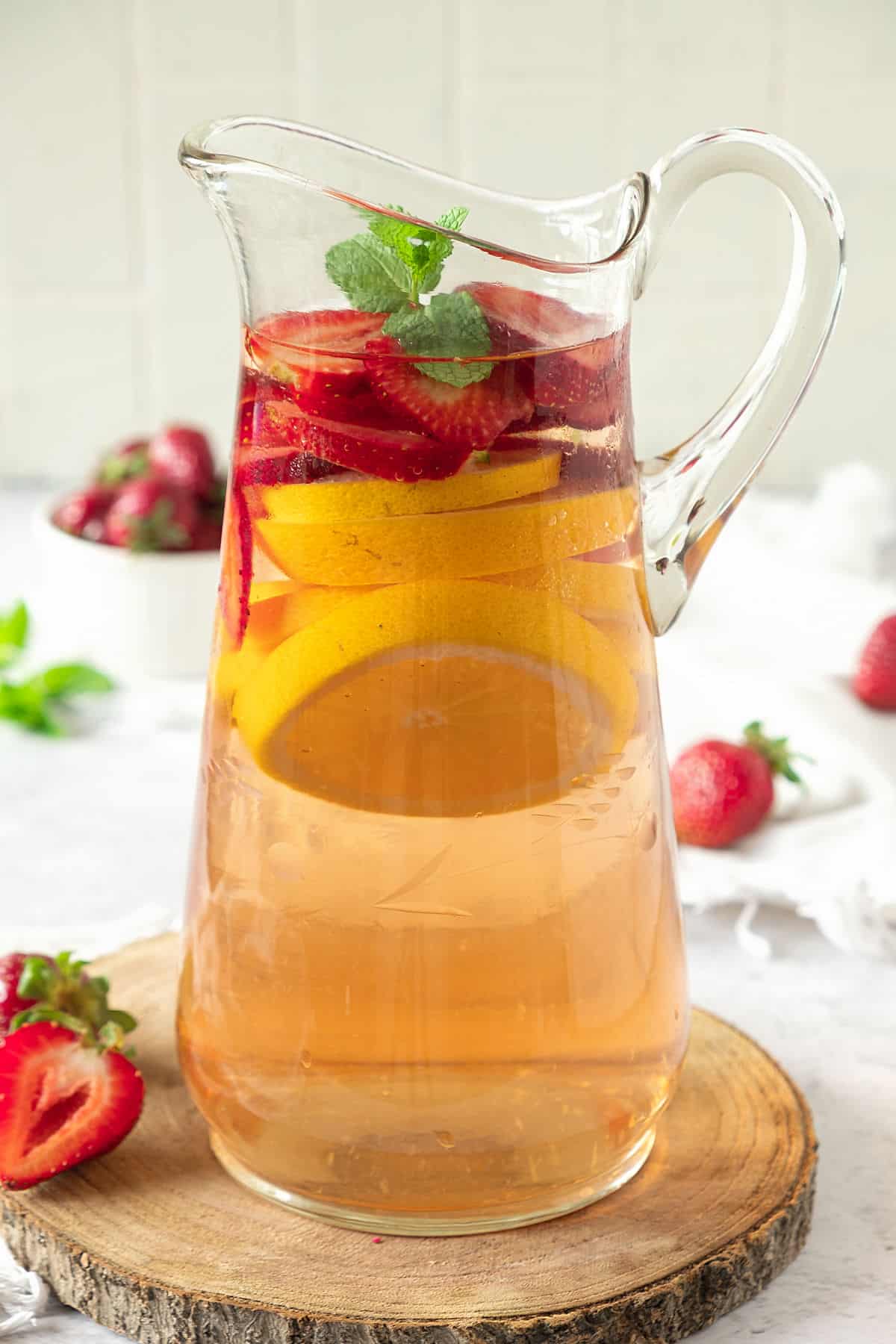 Pitcher of rosé wine sangria with strawberries, citrus slices on a wooden round. Light grey background, fresh strawberries.