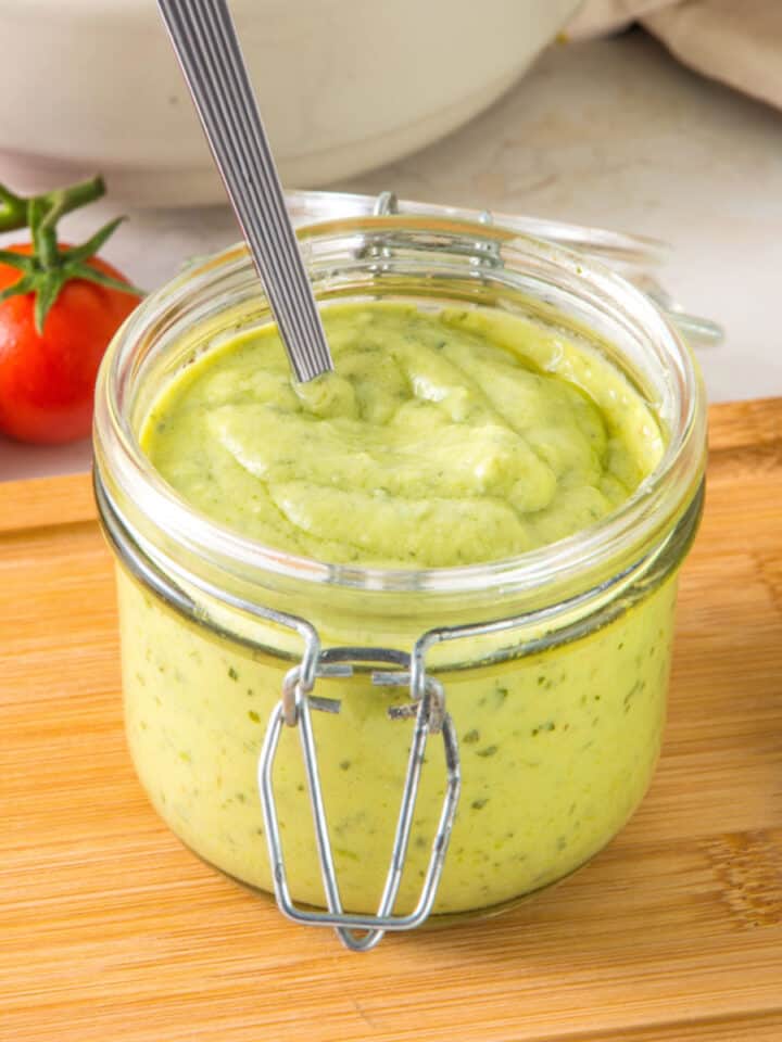 Mason jar with avocado ranch dressing on a wooden table. Tomatoes in white background.