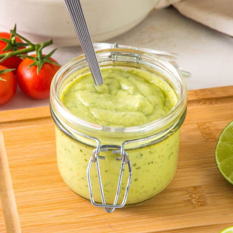 Mason jar with avocado ranch dressing on a wooden table. Tomatoes in white background.
