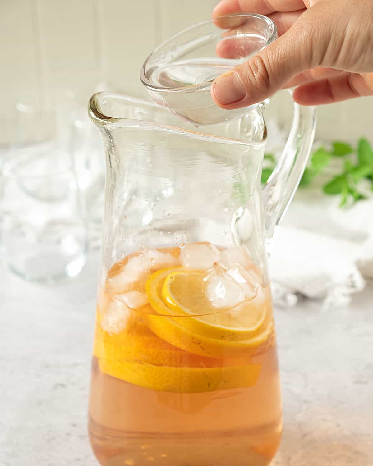 Adding clear syrup to a pitcher with rosé wine, citrus slices and ice. Light background with glasses.