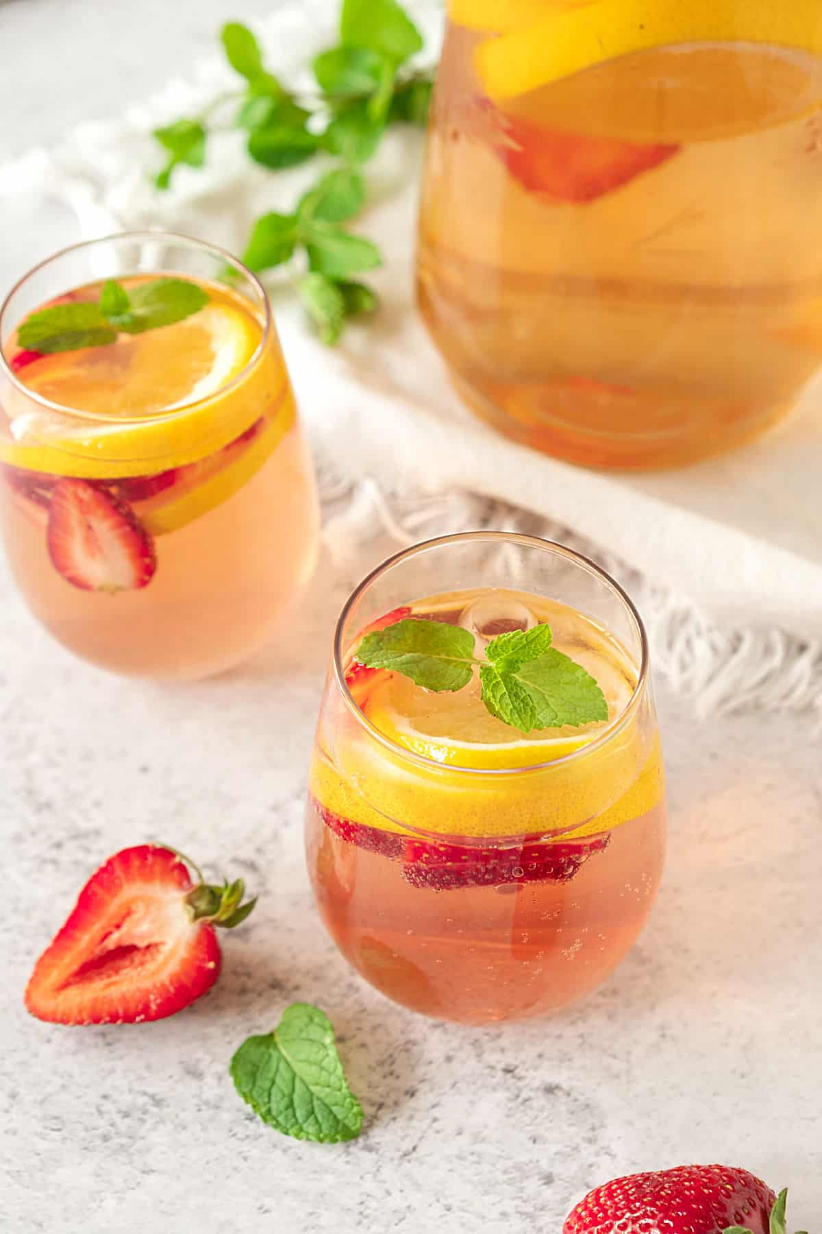 Top view of glasses with rose wine sangria, light grey surface, mint leaves and strawberries. 