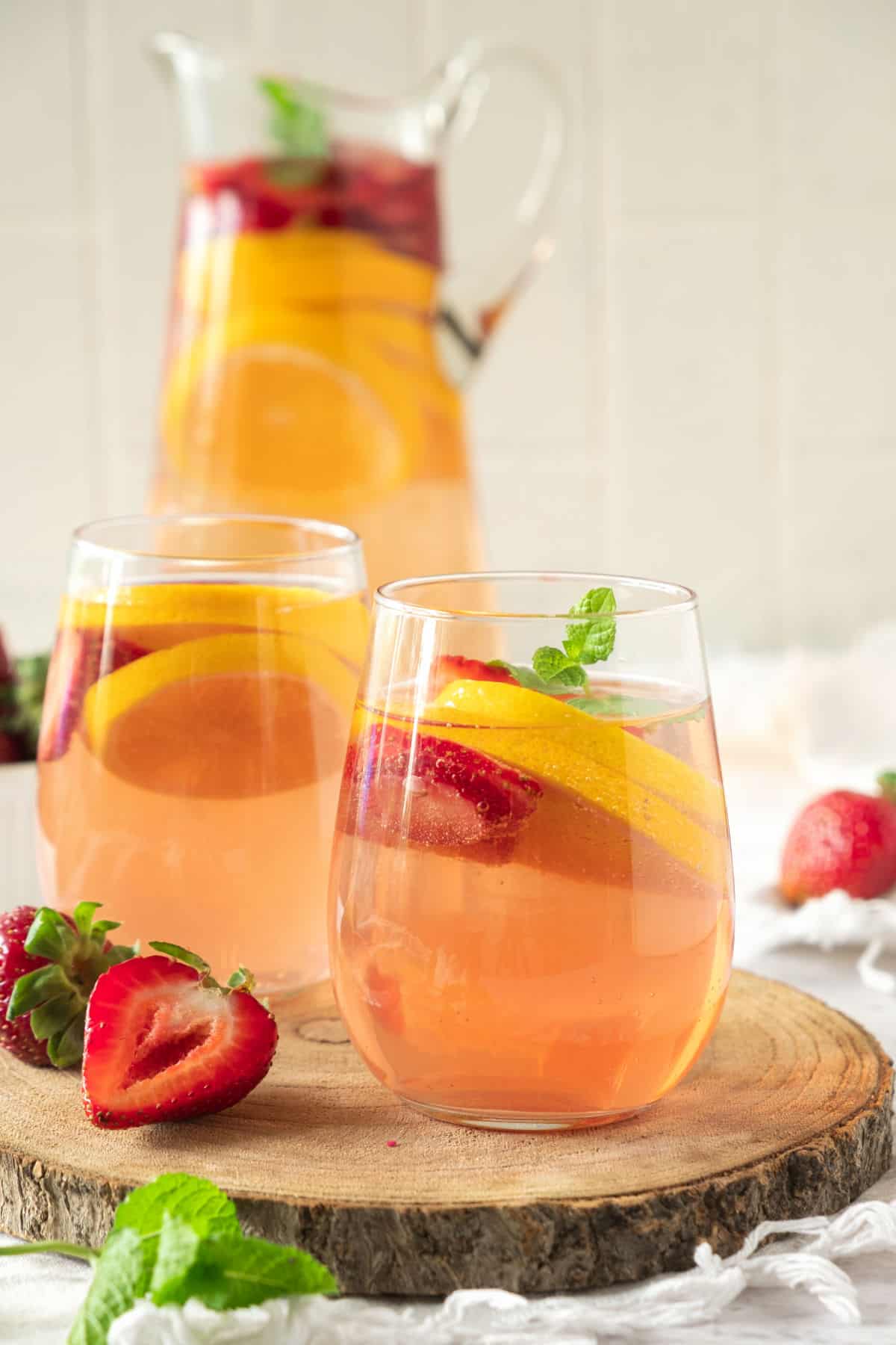 Light grey background with pitcher of rose sangria. Two served glasses on a wood round. 