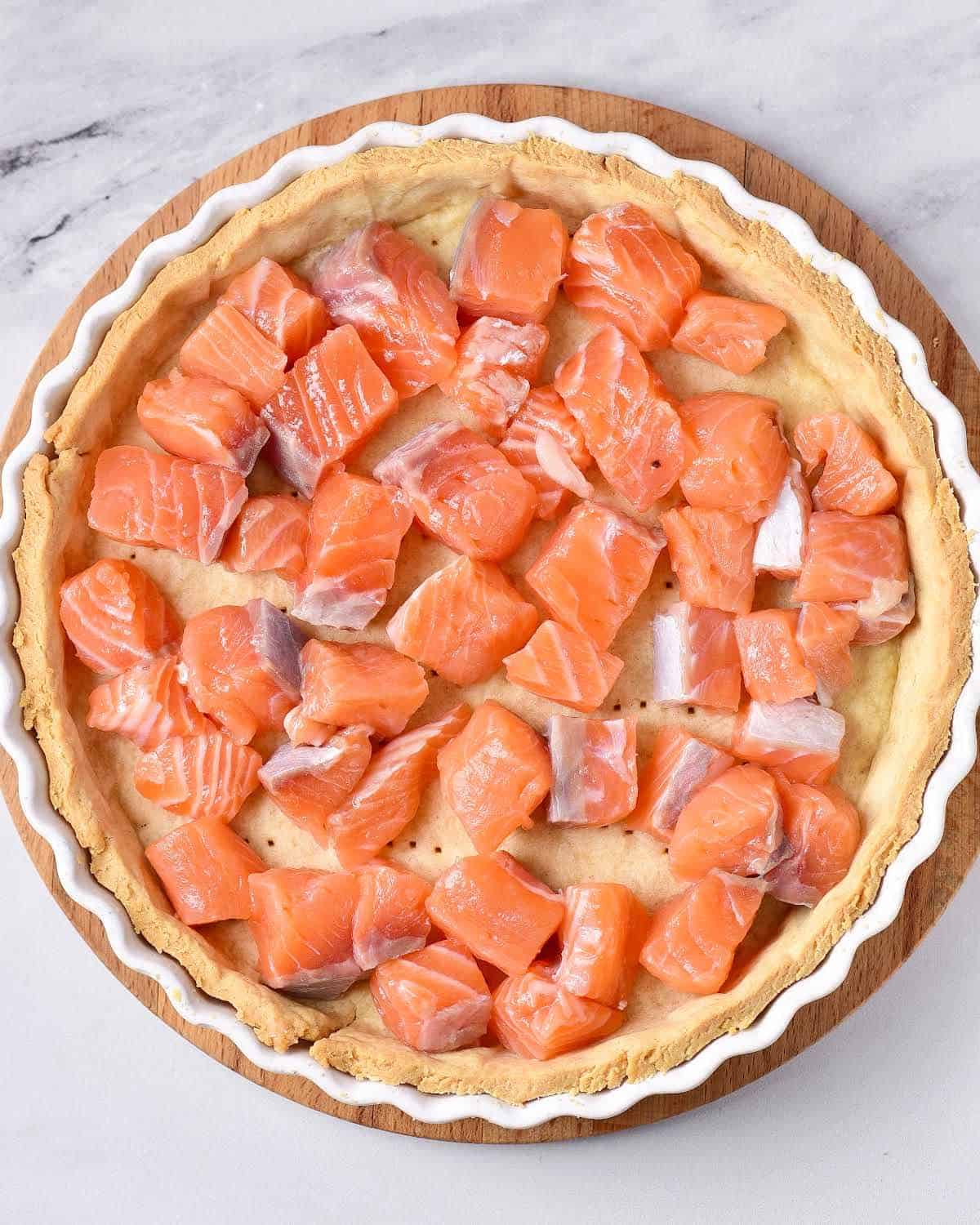 Raw salmon pieces in an unbaked crust on a white marbled surface.