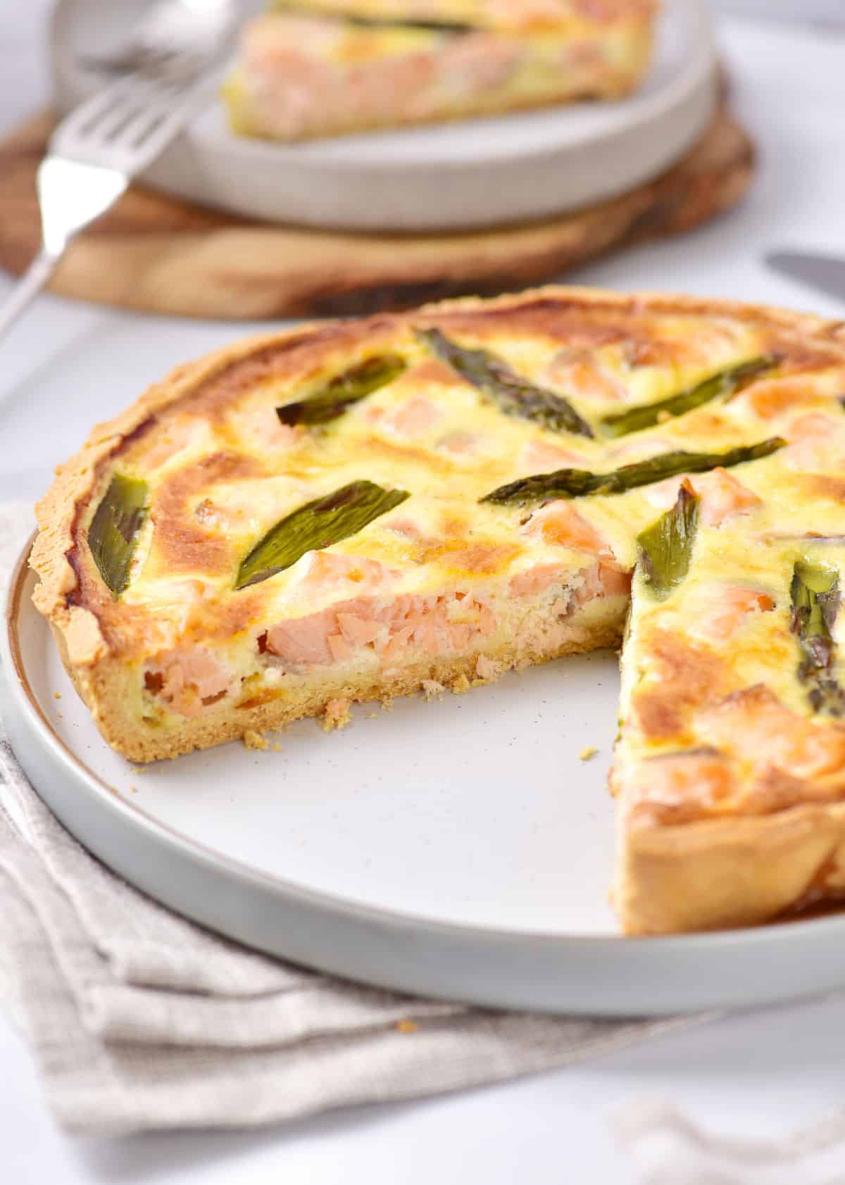 Partial salmon tart on a grey plate with grey kitchen towel. White surface.