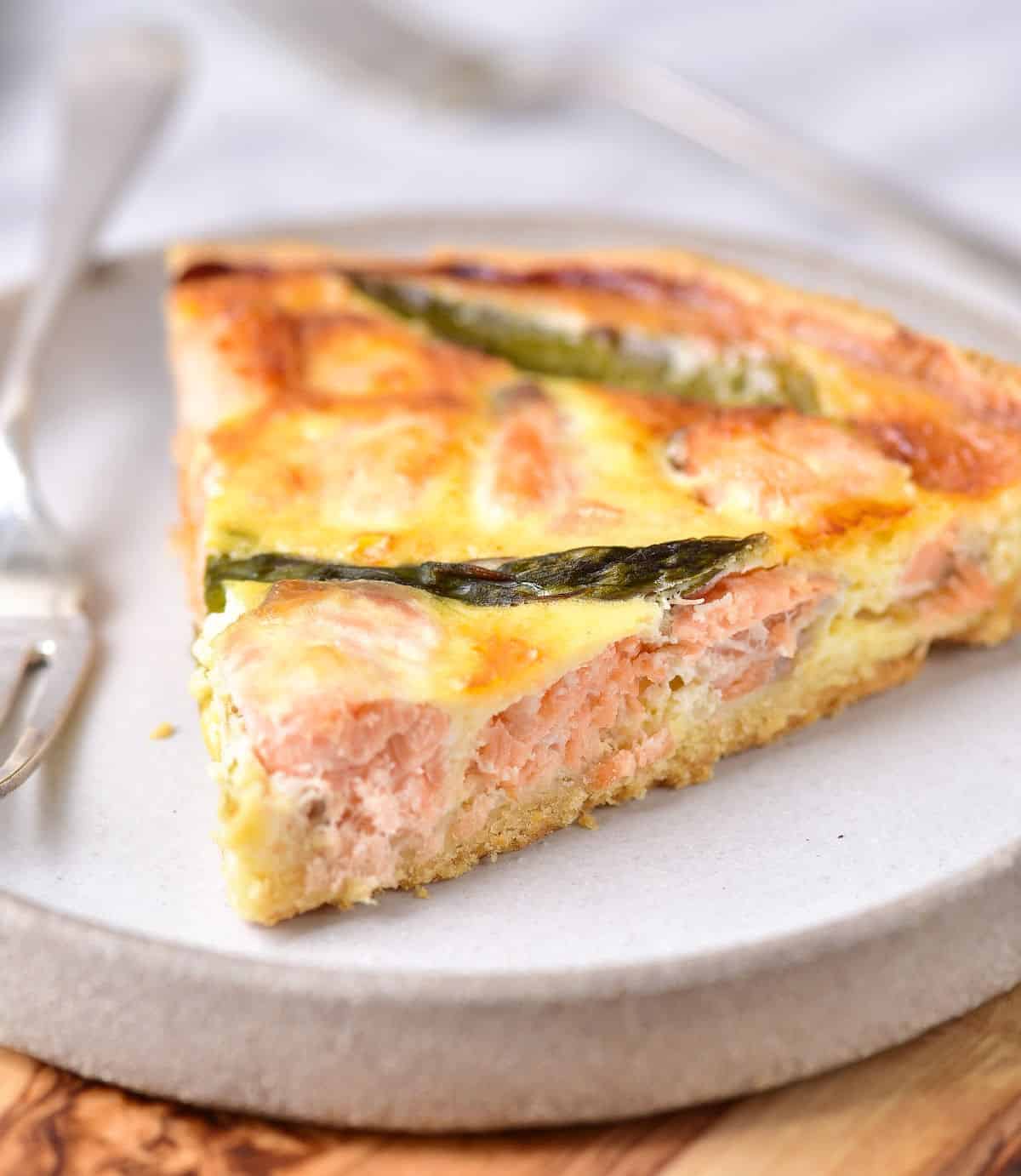 Close up view of salmon quiche slice on a grey plate with a silver fork.