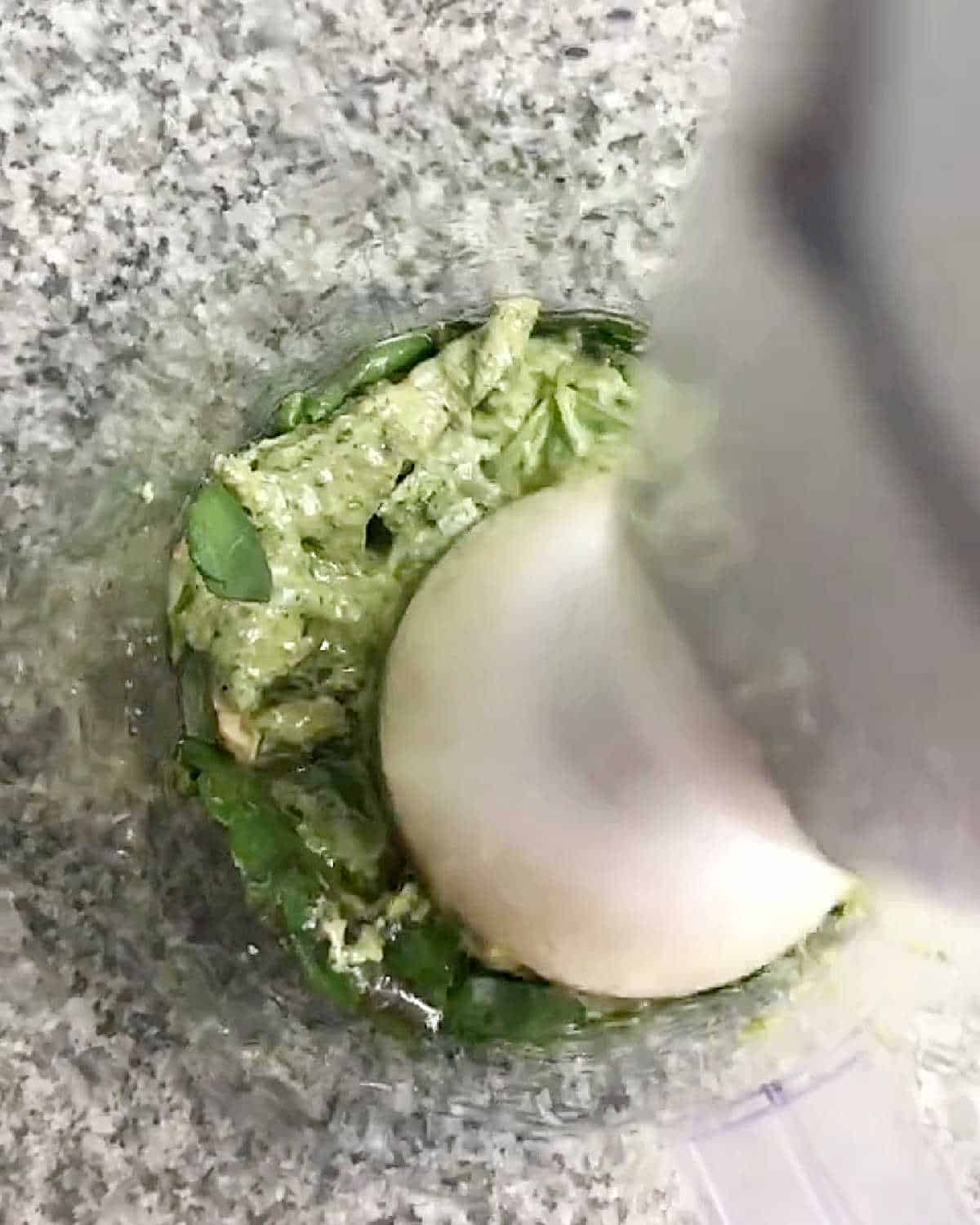 Processing salsa verde with immersion blender in a glass jar on grey granite surface.