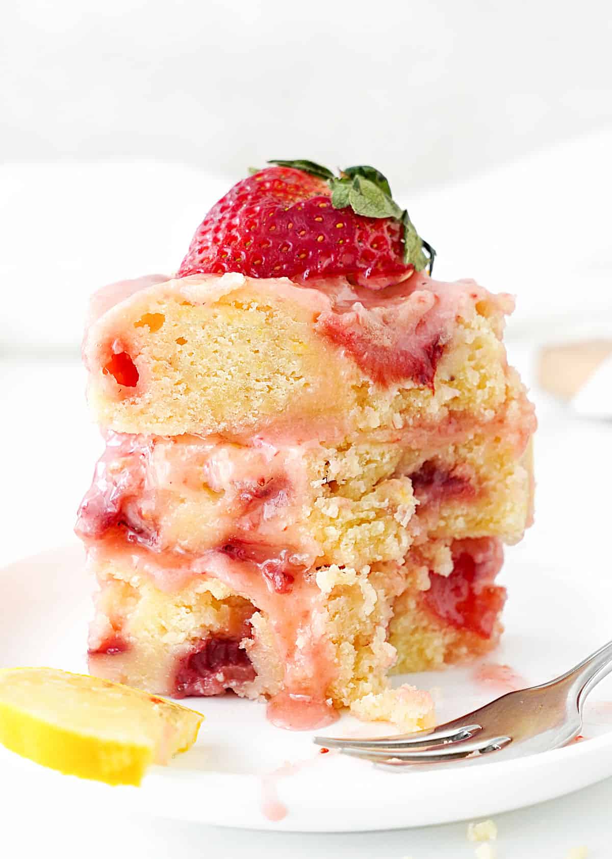 Three bitten glazed lemon strawberry blondies in a stack. White plate and background. 