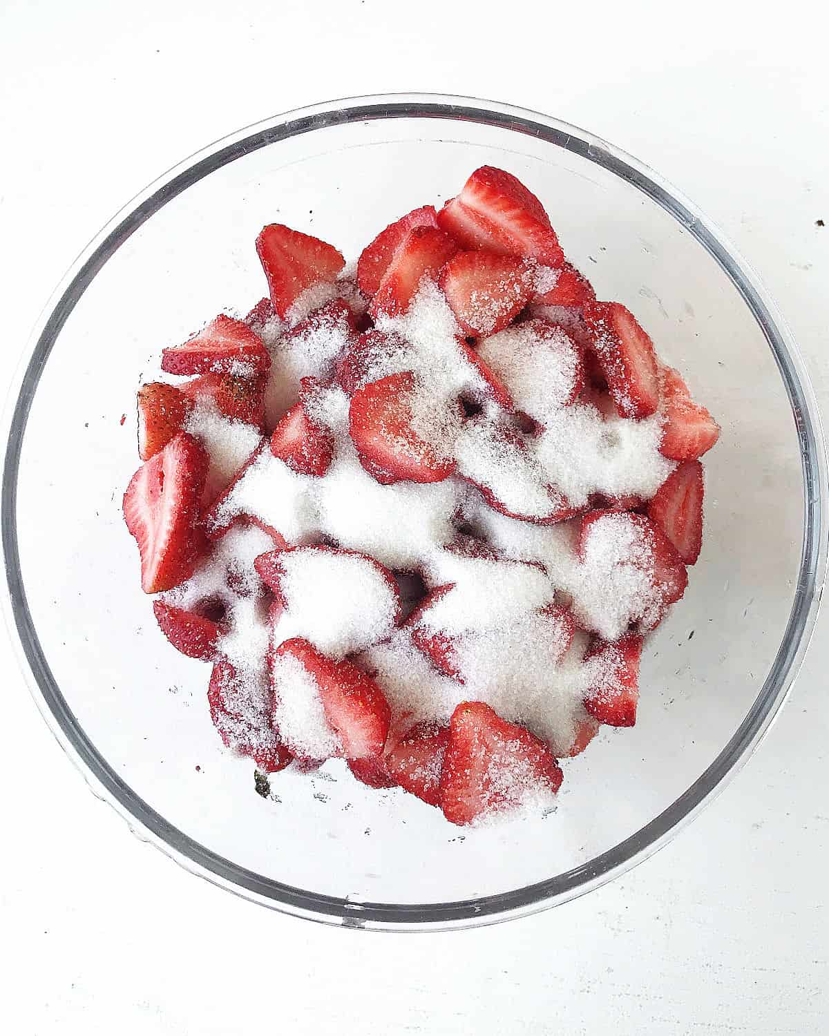 Glass bowl with strawberry pieces and sugar. White background.