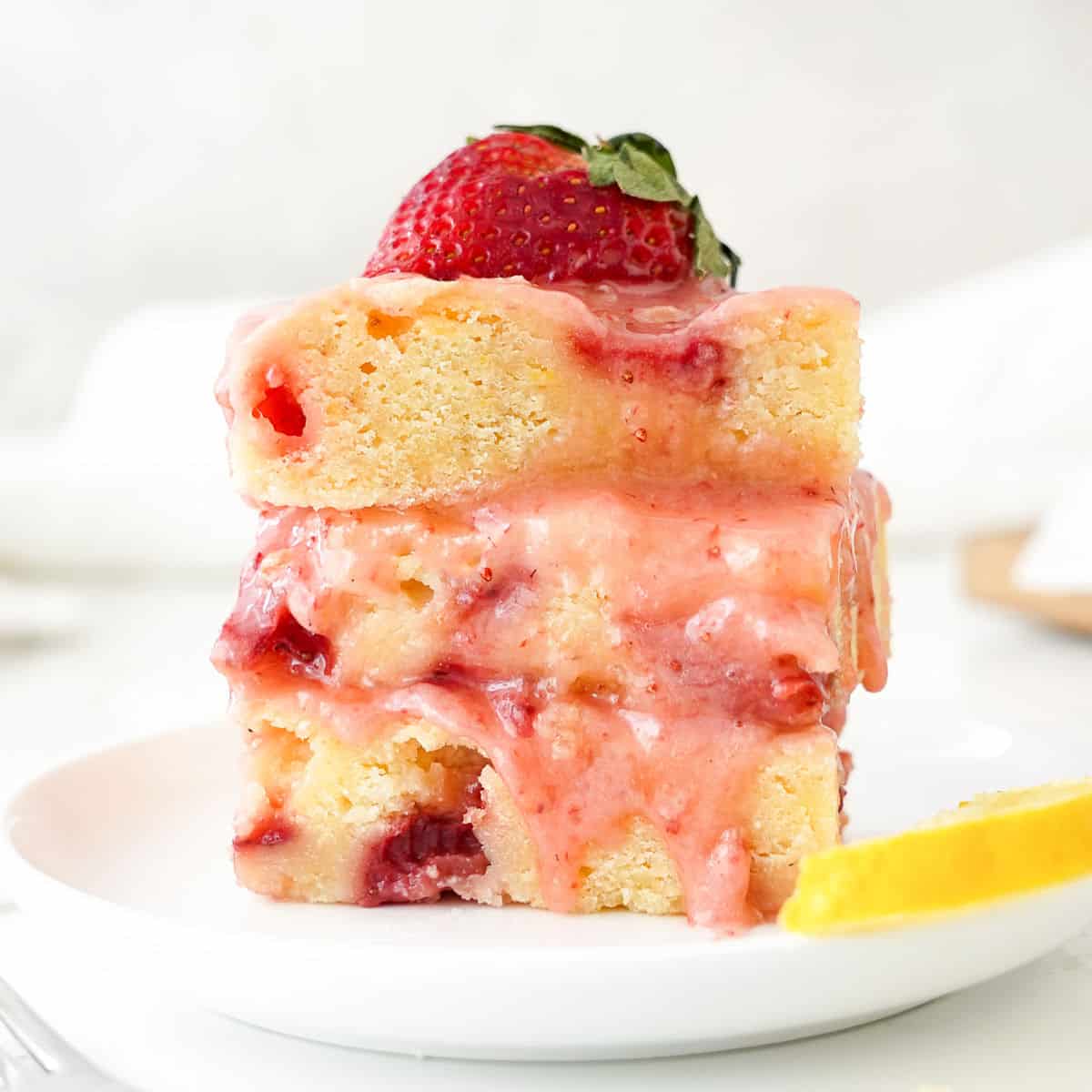 Stack of three glazed strawberry blondies on a white plate. Grey and white background.