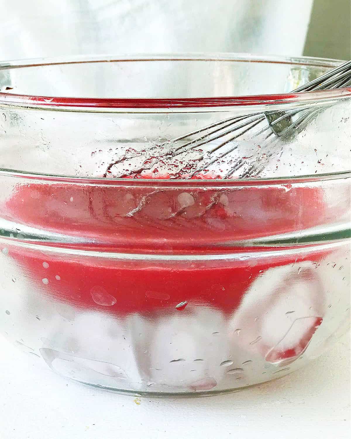 Glass bowl with strawberry syrup whisked over ice in a glass bowl.