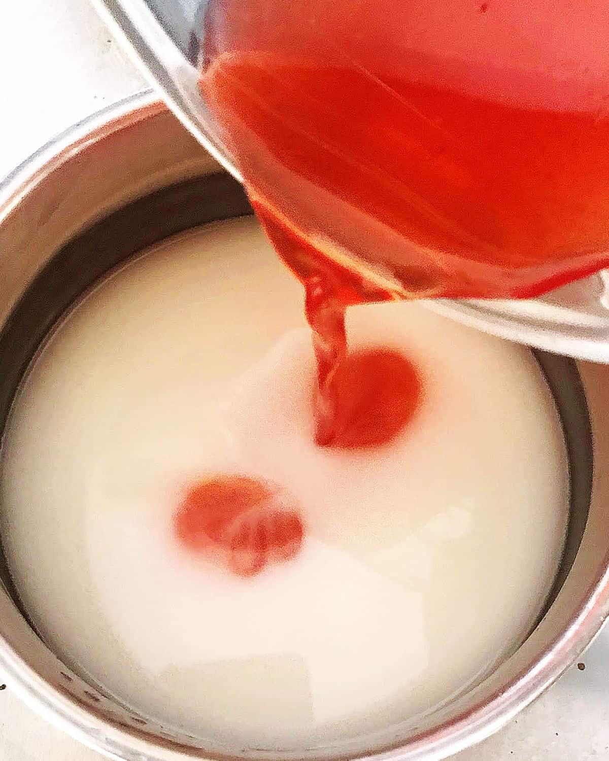 Strawberry jello syrup added to cornstarch slurry in a metal saucepan.