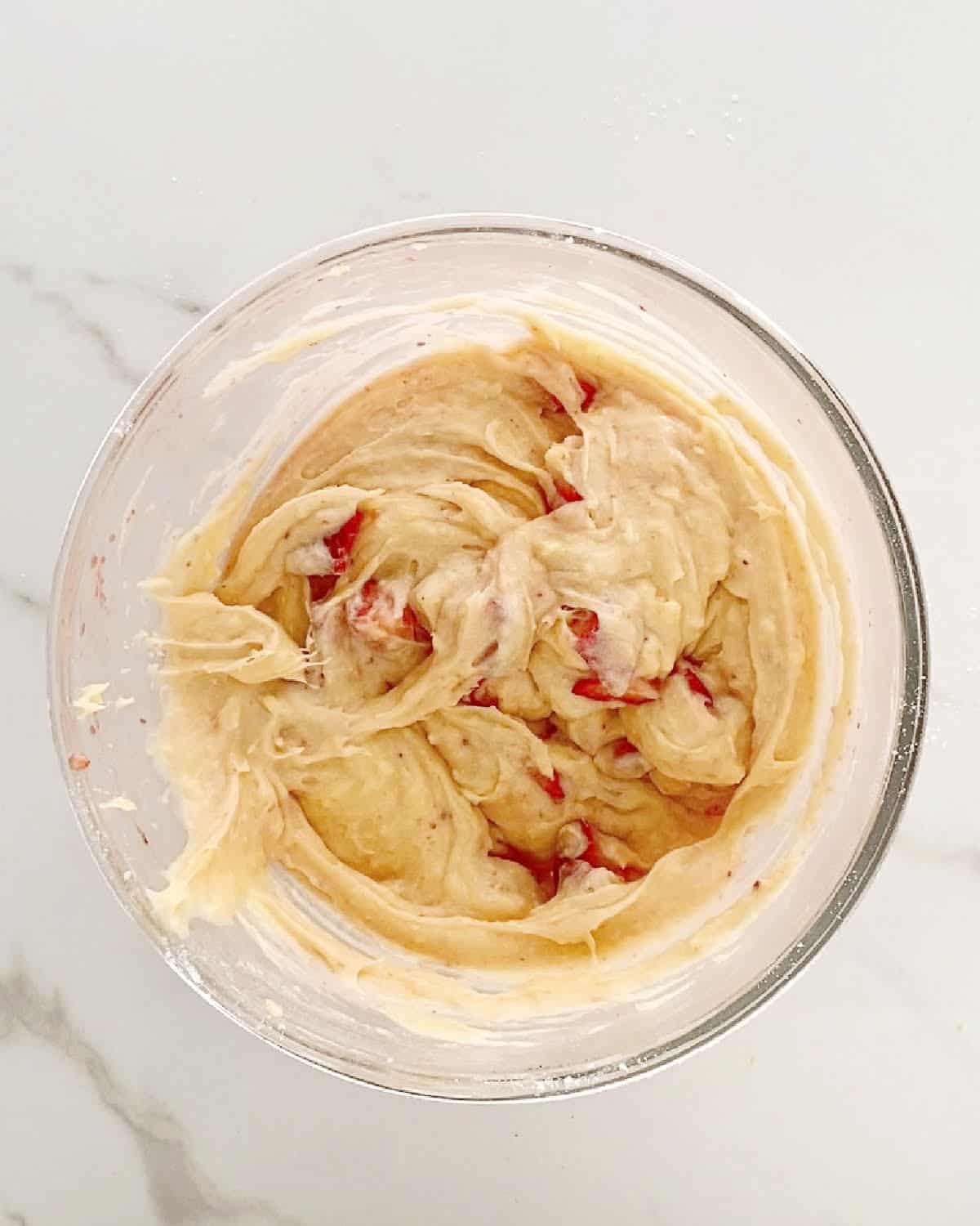 Glass bowl with lemon strawberry blondie batter on a white marbled surface.