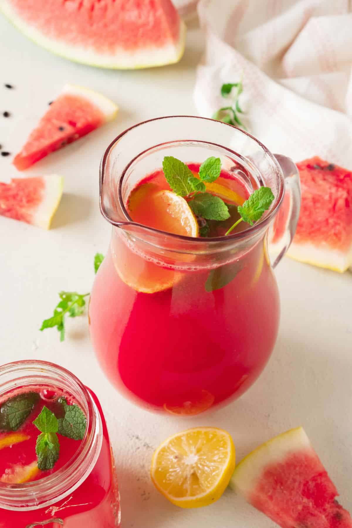 Watermelon pieces surrounding a pitcher of watermelon lemonade with mint leaves.