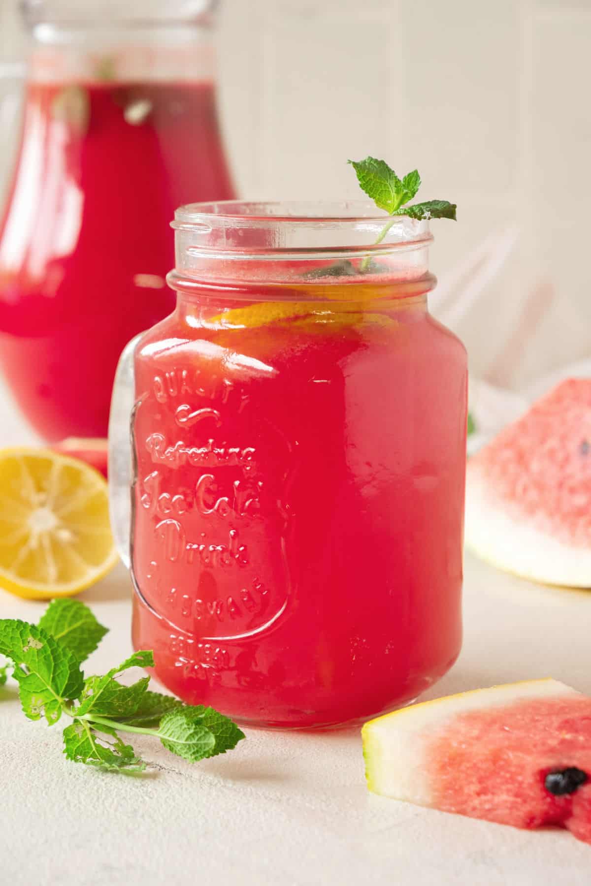 Watermelon lemonade in a small jug and a pitcher. Mint sprigs, lemon slices, white background. 