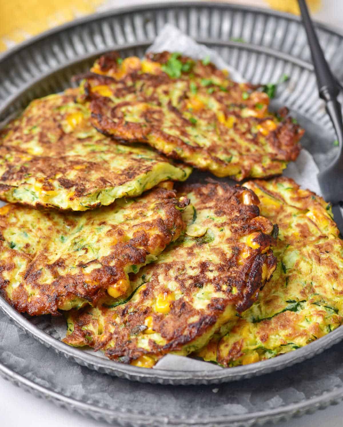 Metal plate with five overlapping zucchini corn fritters. 