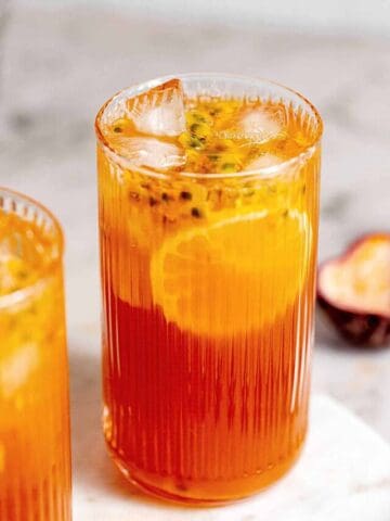 Tall glass of passionfruit tea on a marble board with grey background.