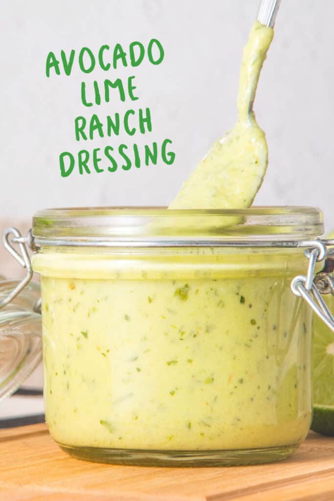 Green text overlay on mason jar with spoon and avocado ranch dressing. Wooden board, grey background.
